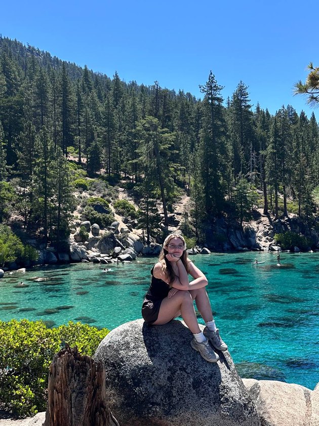 Diana sitting on a boulder by the turquoise water of Lake Tahoe