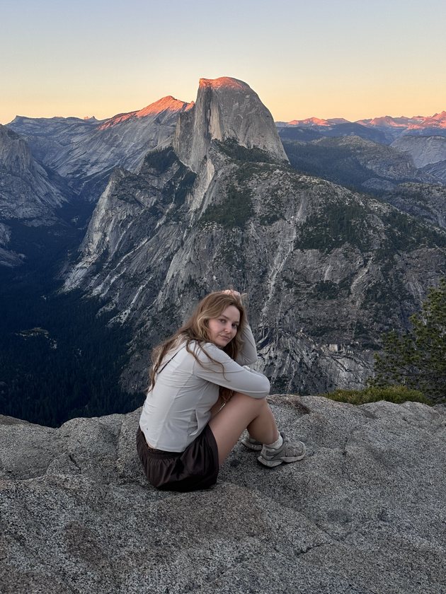 Diana sitting on a granite ledge at Glacier Point with Half Dome glowing at sunset behind her